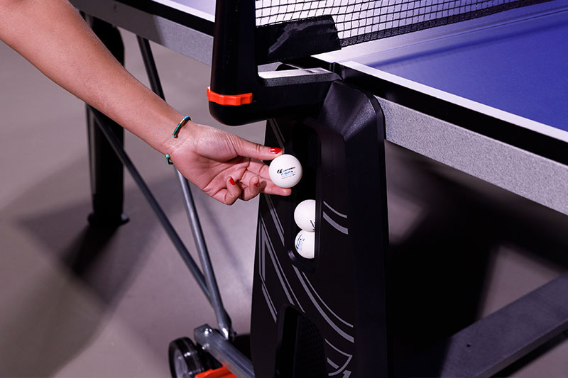 main qui range une balle dans le flanc d'une table de ping pong Cornilleau 500 indoor